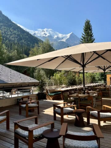 Outdoor dining area with shade umbrellas over tables and chairs and view of Mont Blanc in the distance.