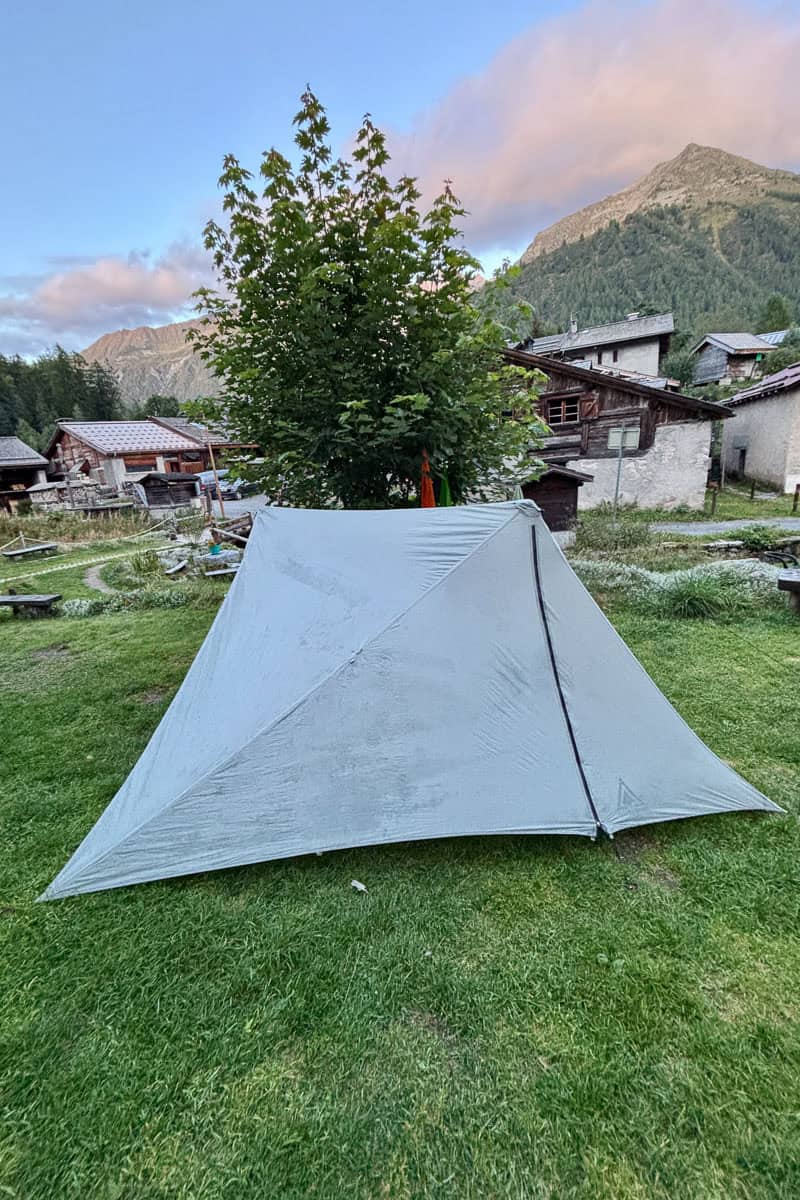 Backpacking tent pitched in front of several small buildings.