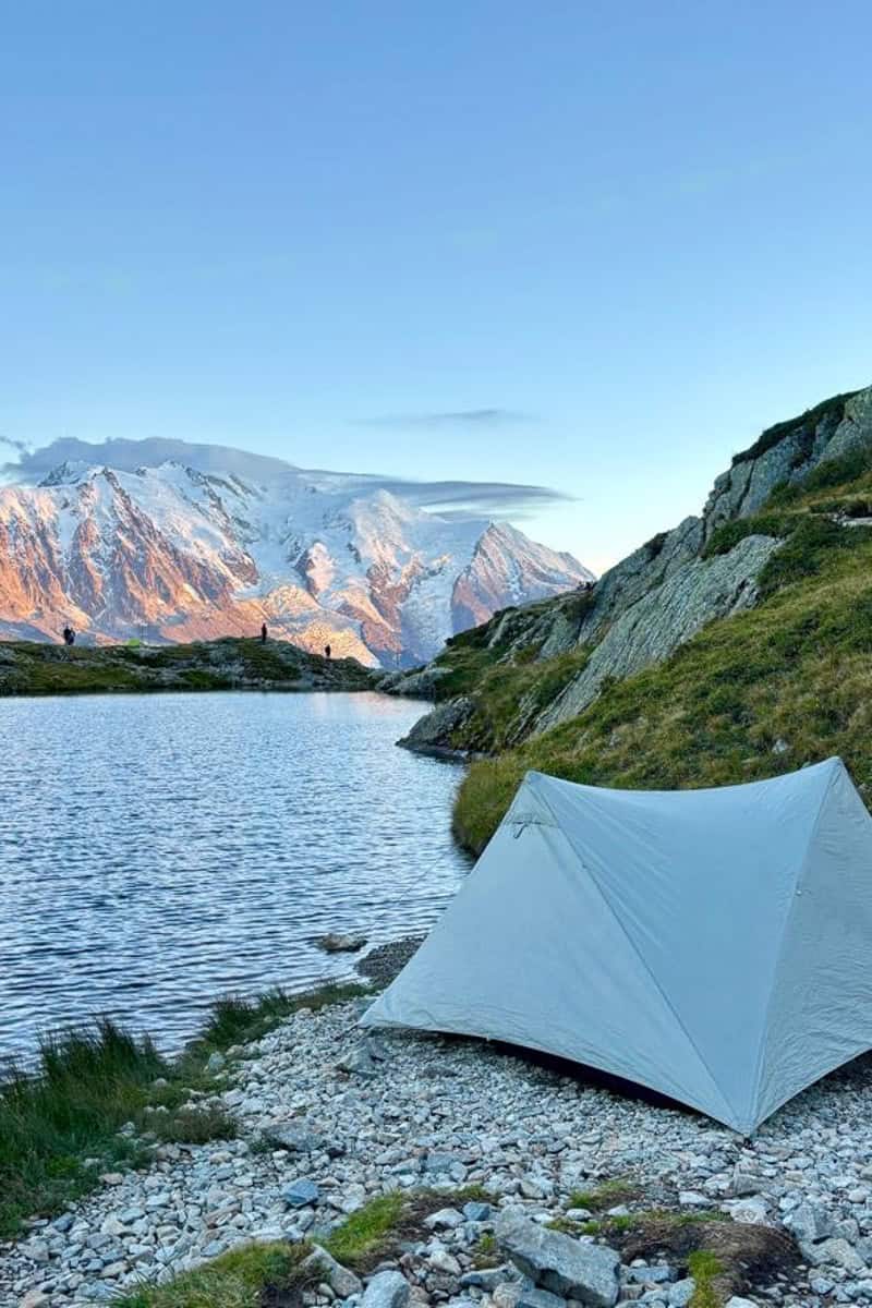 Tent pitched on edge of lake with snow-covered mountains on the other side.