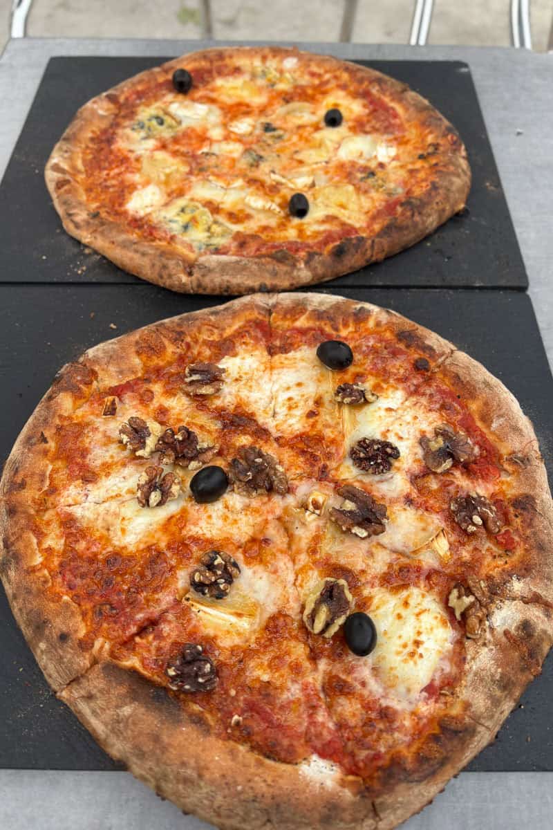 Two pizzas topped with nuts and olives.