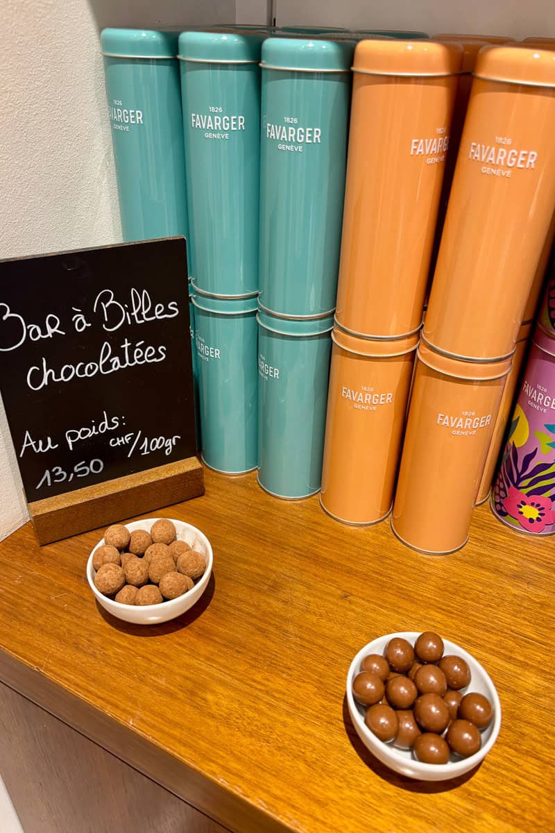 Two dishes full of chocolate balls in front of tins stacked for sale.