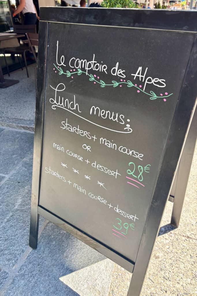 Display board advertising lunch prices outside Les Comptoir des Alpes.