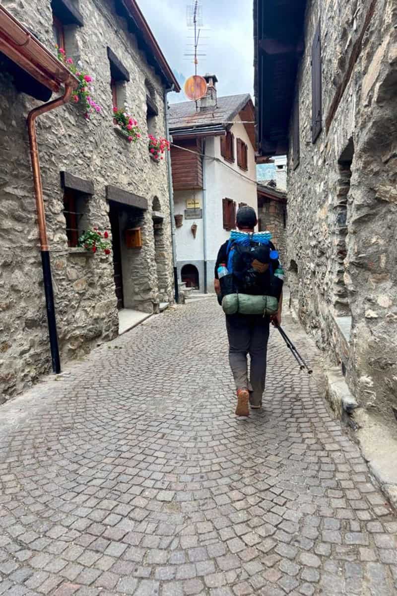 Backpacker walking down cobbled street in Courmayeur, Italy.