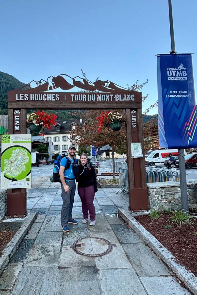 A couple standing under a decorative gateway marking the start of the Tour du Mont Blanc.
