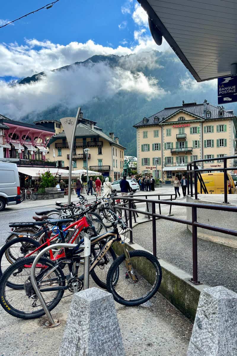 Bicycles parked along street in Chamonix with view of mountain and clouds in background.