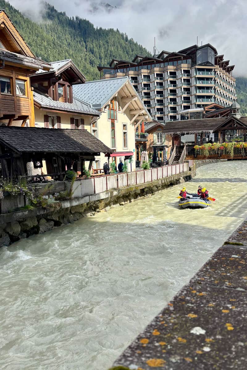 River through Chamonix with homes along its border and a group in a raft floating in the center.