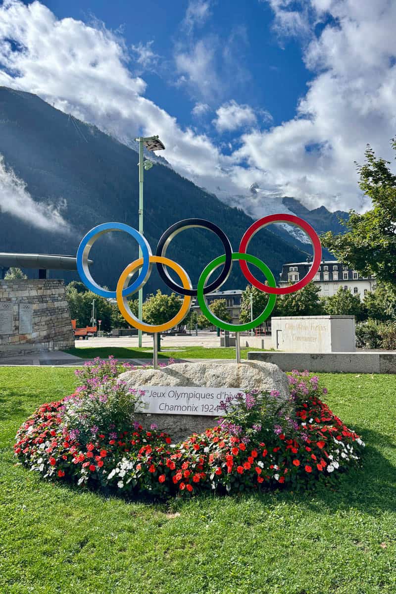 Olympics rings displayed above flowerbed in Chamonix park.