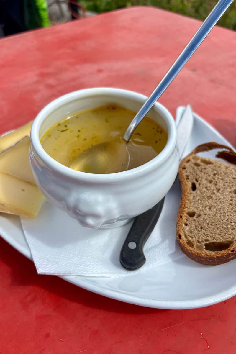 Cup of bone broth served with slice of brown bread and cheese.