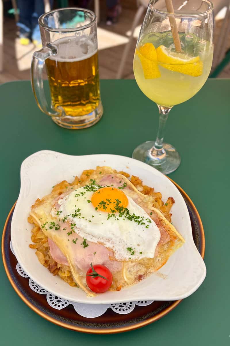 Swiss rosti, a potato cake topped with egg, on a plate next to a glass of limoncello spritz and a glass of beer, among our favorite food and drink on the Tour du Mont Blanc.