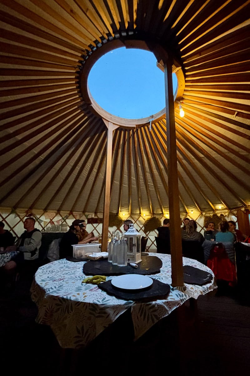 Dining area under yurt, with center area open to the sky, with diners enjoying some of the best food and drink on the Tour du Mont Blanc.