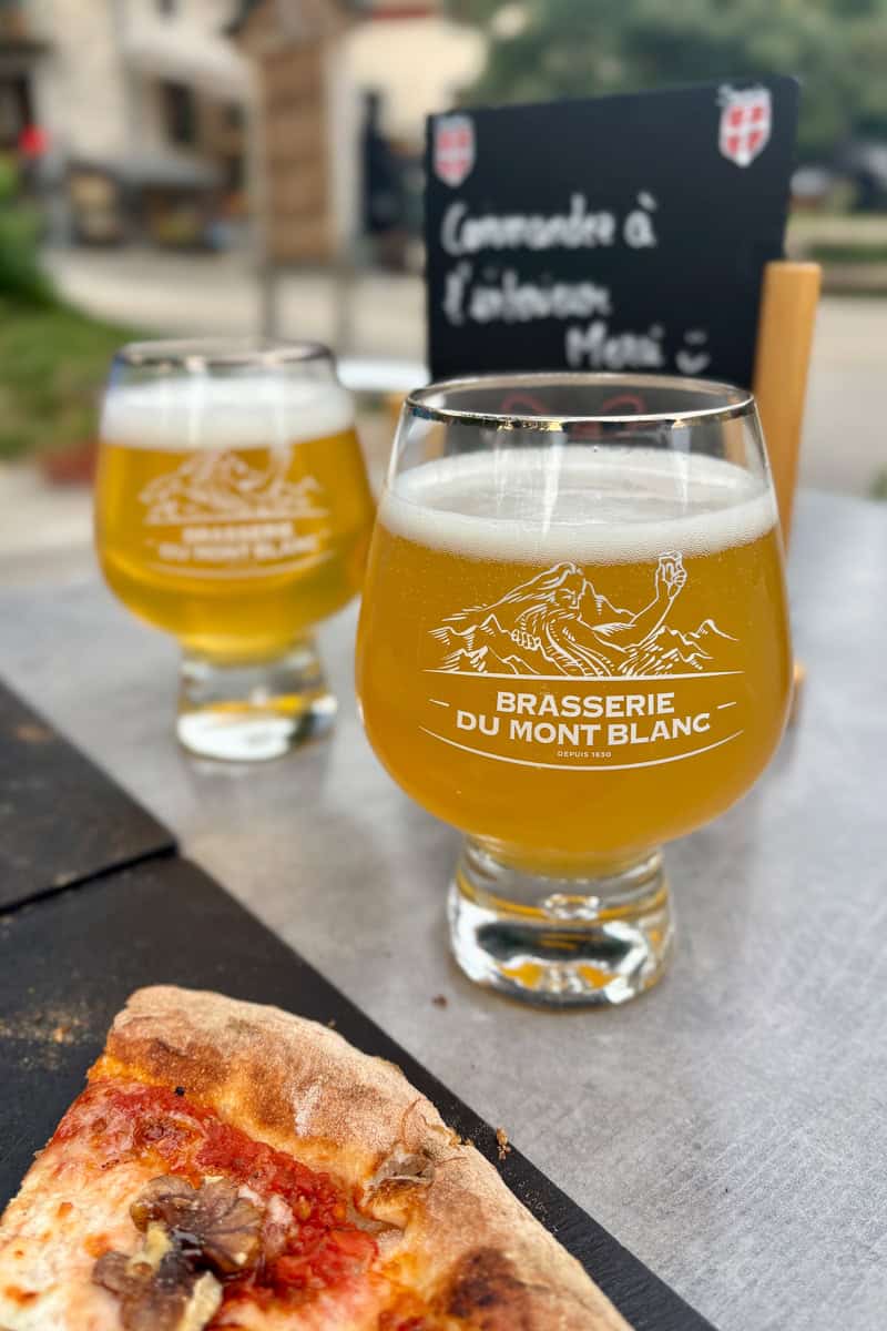 Two glasses of beer next to edge of pizza, some of the best food and drink on the Tour du Mont Blanc.