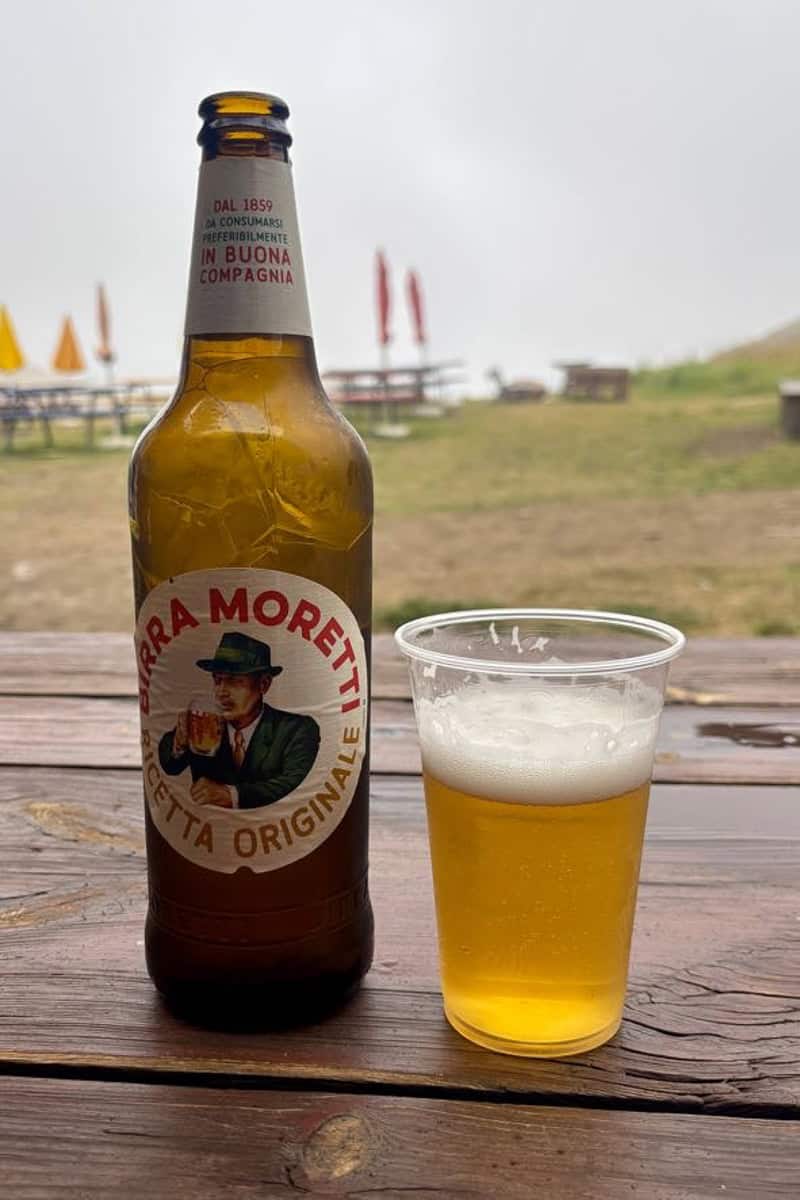 Bottle of Birra Moretti beer with some poured into plastic cup.