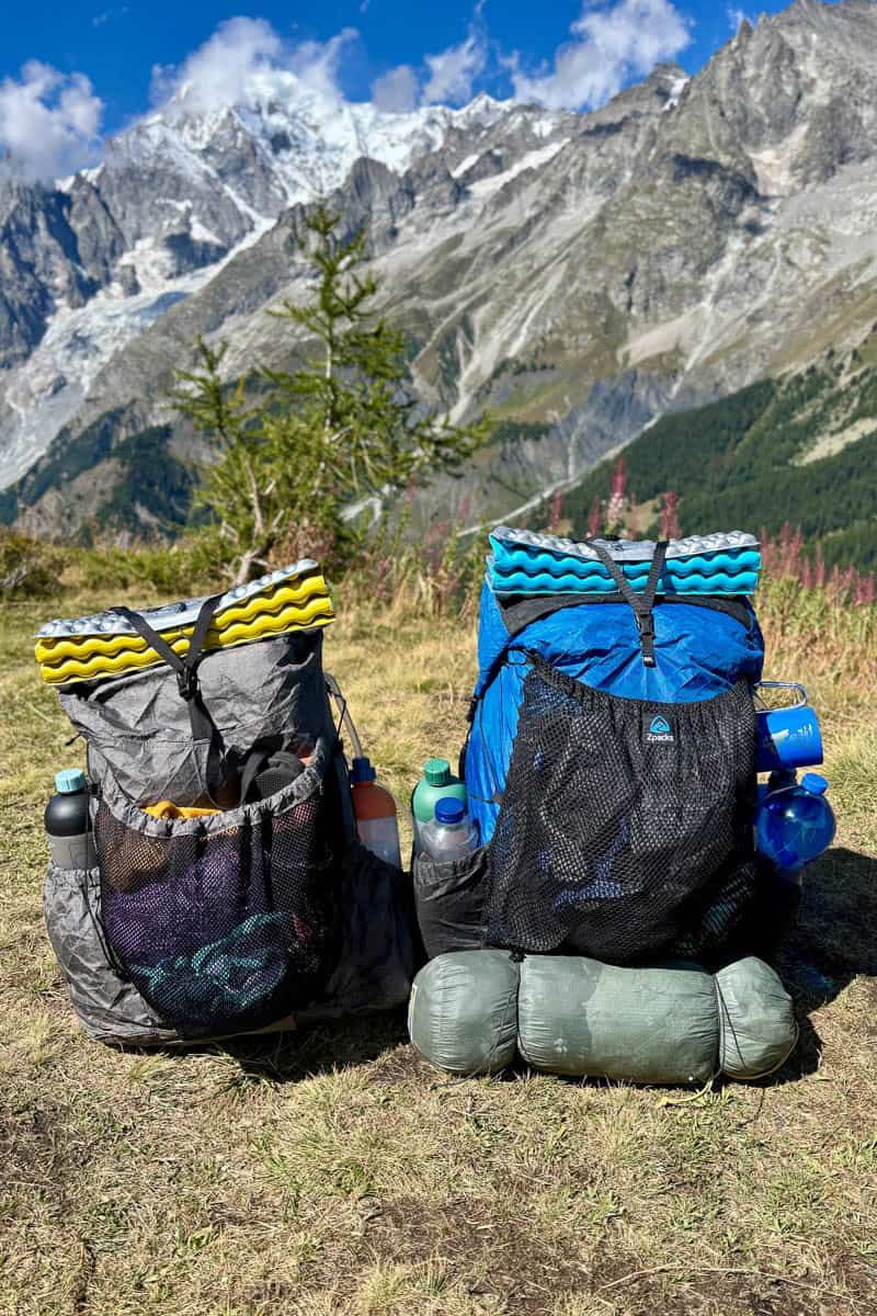 Two backpacks loaded with gear for the Tour du Mont Blanc set on ground with mountains in background.