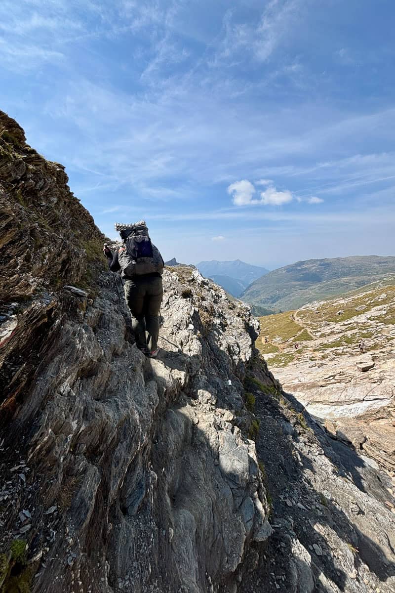 Hiker navigating narrow rocky ledge on mountainside on the Tour du Mont Blanc.