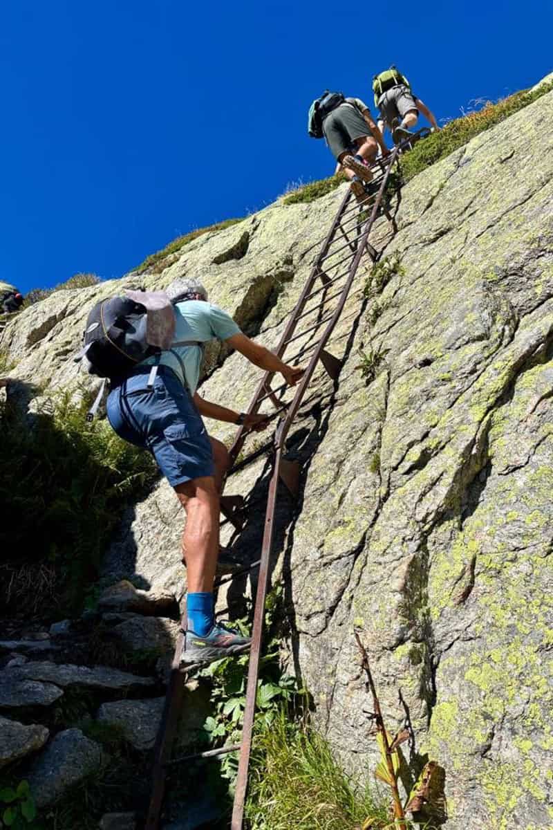 View from below of hikers climbing metal ladders on cliff face.