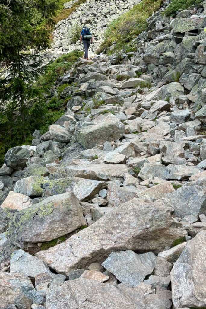 Hiker navigating rocky avalanche field on Stages 10 and 11 of the Tour du Mont Blanc.