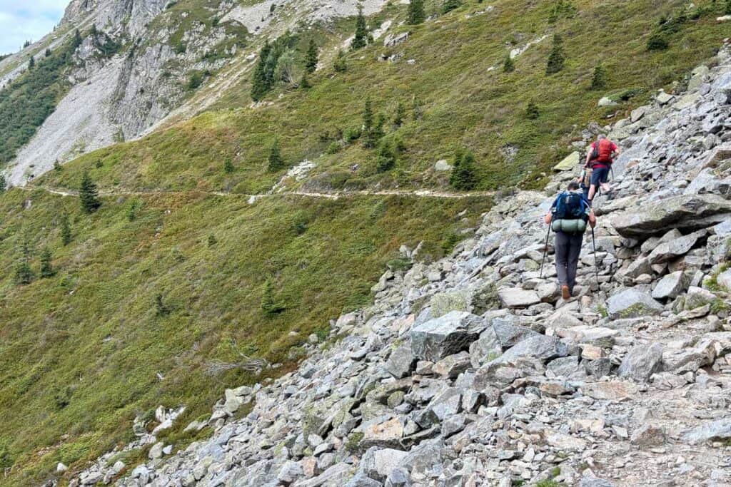 Hikers navigating rock avalanche fields on mountainside.