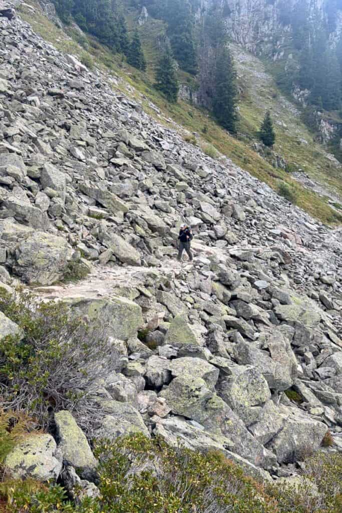 Hiker following trail through rock avalanche field on mountainside.