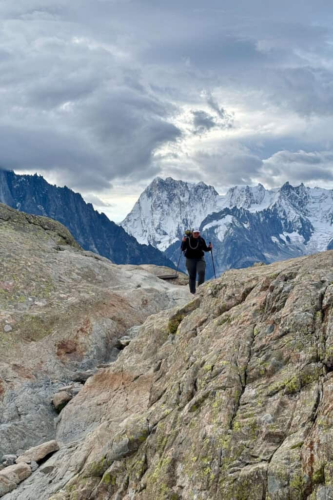 Hiker navigating rocky terrain with snowy mountains in background on Stages 10 and 11 of the Tour du Mont Blanc.