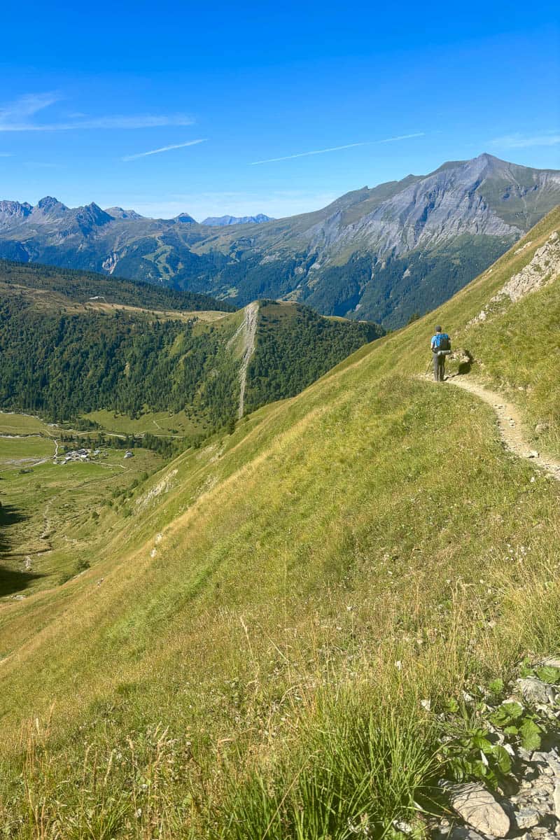 Backpacker pausing on mountainside dirt trail above valley view.