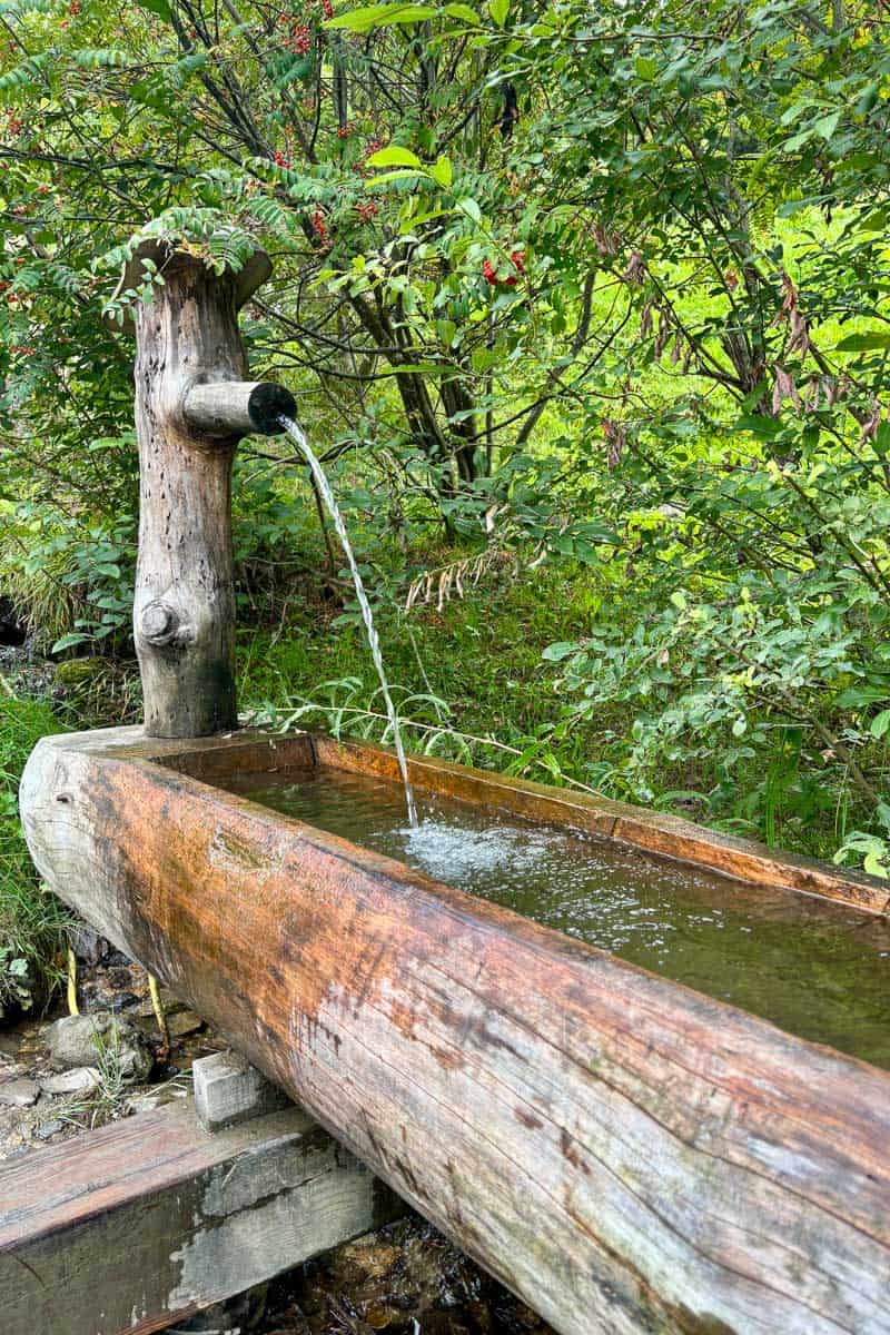 Fountain spouting water into wooden trough along the Tour du Mont Blanc.