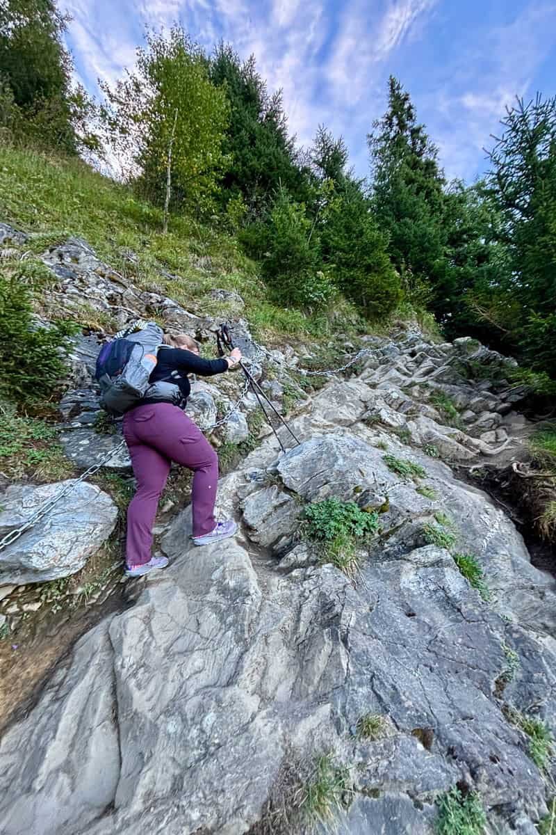 Hiker using trekking poles to navigate rock scramble in Stage 1 of the Tour du Mont Blanc.
