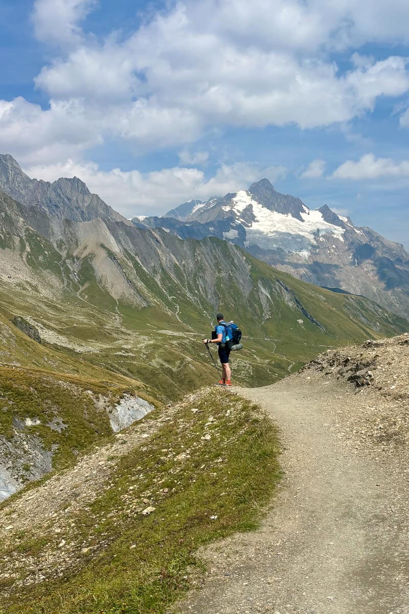 Backpacker standing above Alpine valley viewing mountain peaks.
