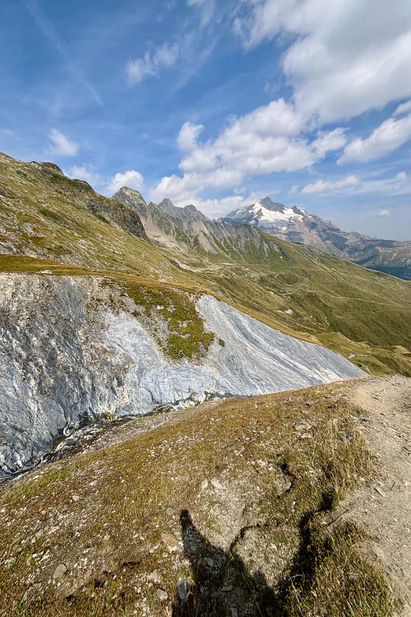 View from trail of snow-covered mountain peak and blue sky.