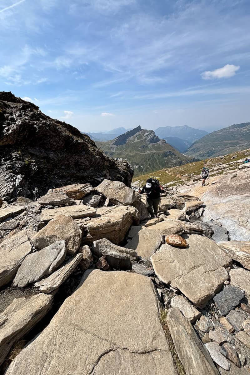 Backpacker navigating steep rock scramble with the help of trekking poles.