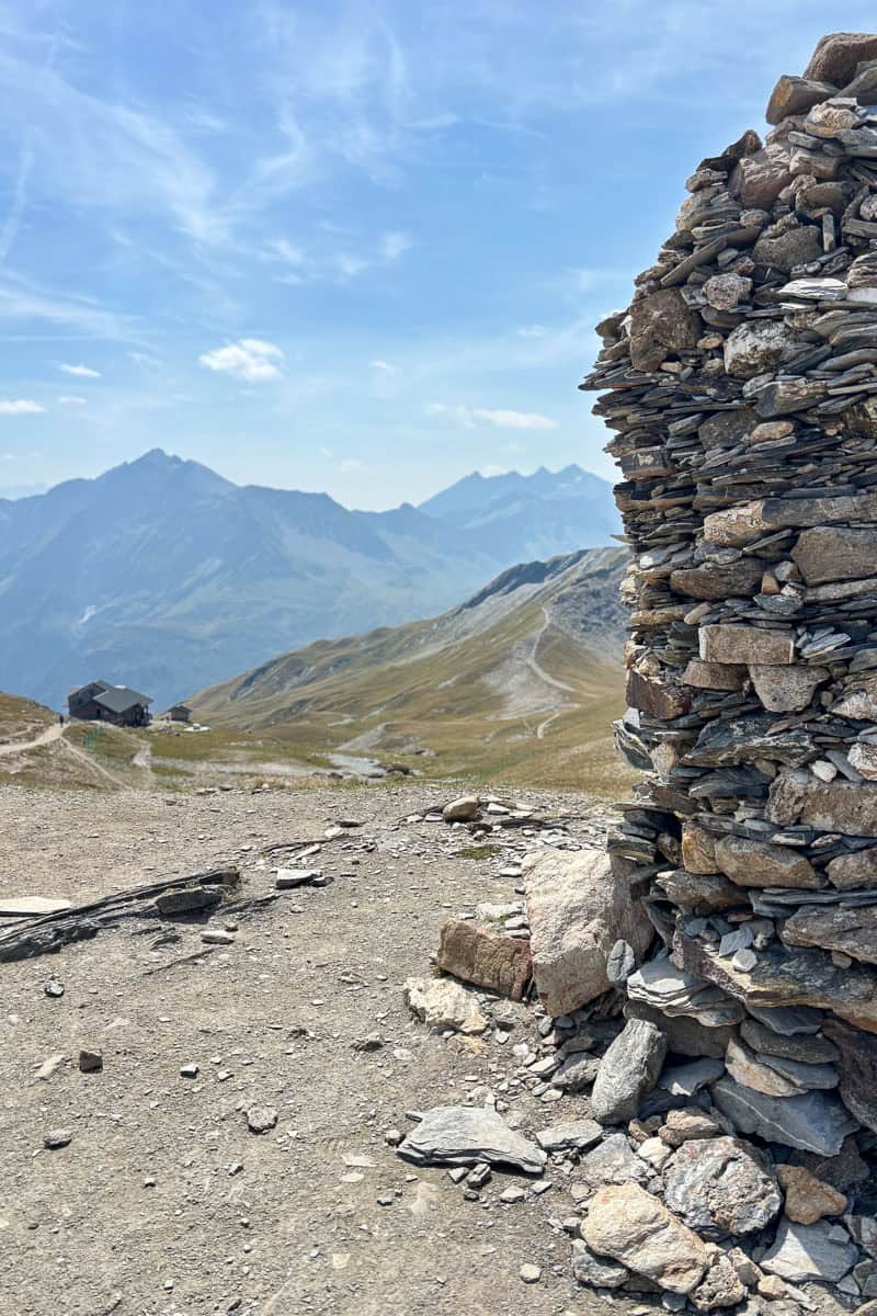 Large trail cairn built of hundreds of rocks, with trail refuge cabin in distance.