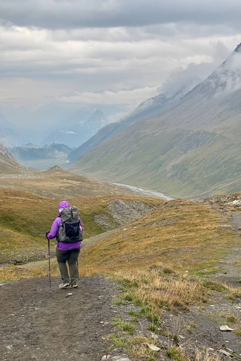 Backpacker dressed for chilly weather navigating down sloped trail.
