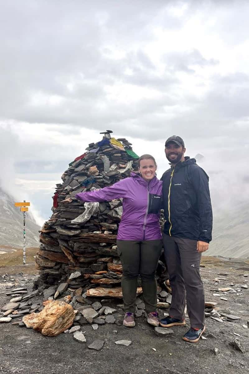 Backpackers posing next to tall rock cairn marking the border between France and Italy.