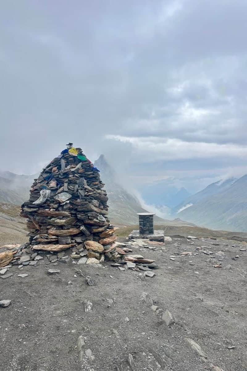 Tall rock cairn in view of mountains shrouded with fog and clouds.