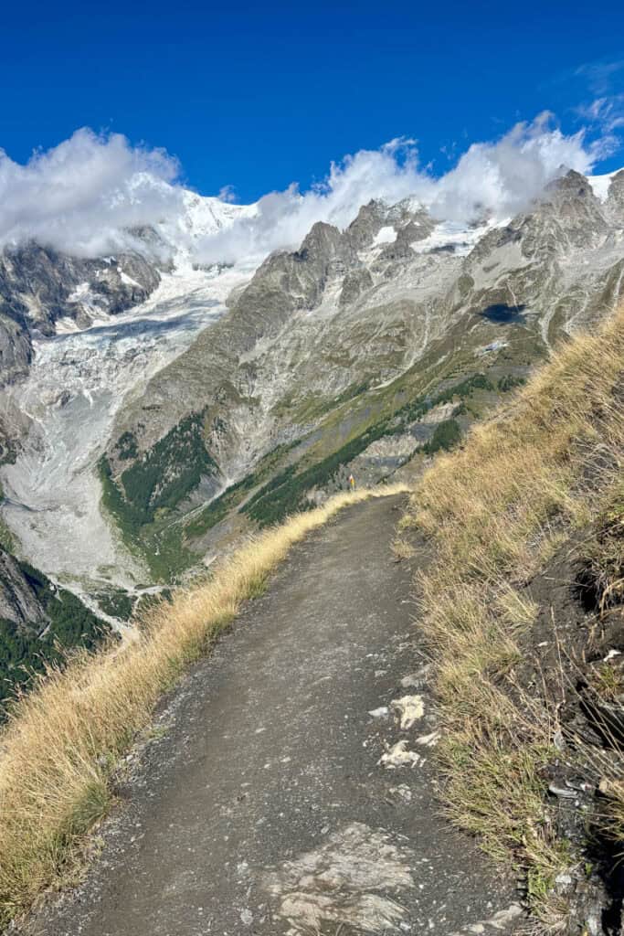 Gravel trail leading towards rugged snow-covered mountains.