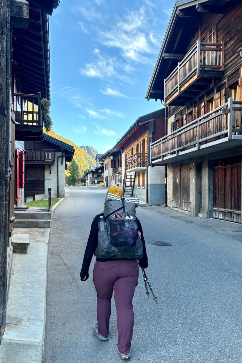 Backpacker walking on road through village to begin Stage 7 of the Tour du Mont Blanc.