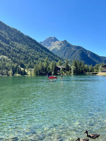 Lake at Champex Lac, with forested mountainsides in view and people on paddleboards in the water.