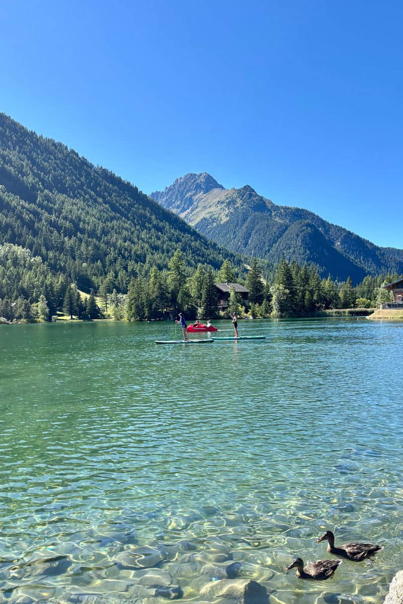 Lake at Champex Lac, with forested mountainsides in view and people on paddleboards in the water.