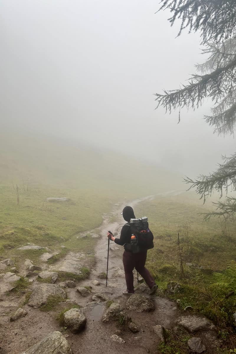Backpacker traversing muddy trail through foggy landscape on Stage 8 of the Tour du Mont Blanc.