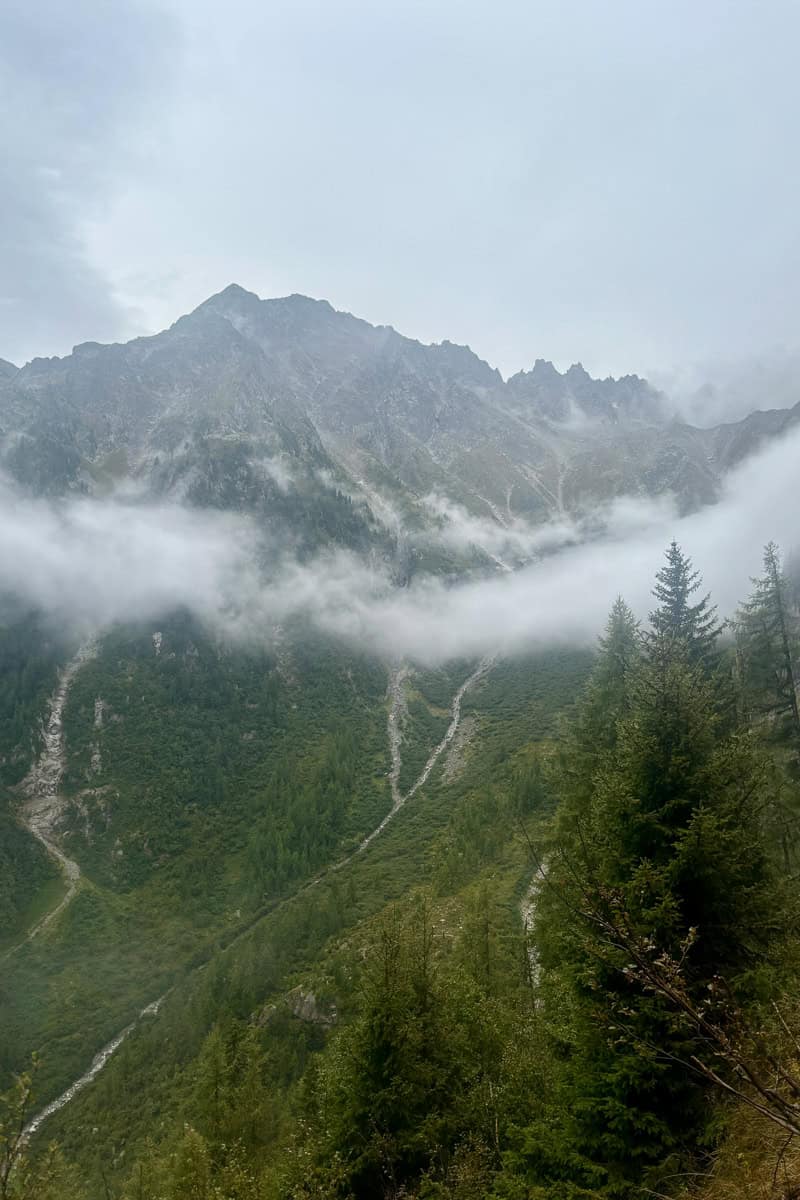 Trail down steep mountainside with cloud cover drifting across.
