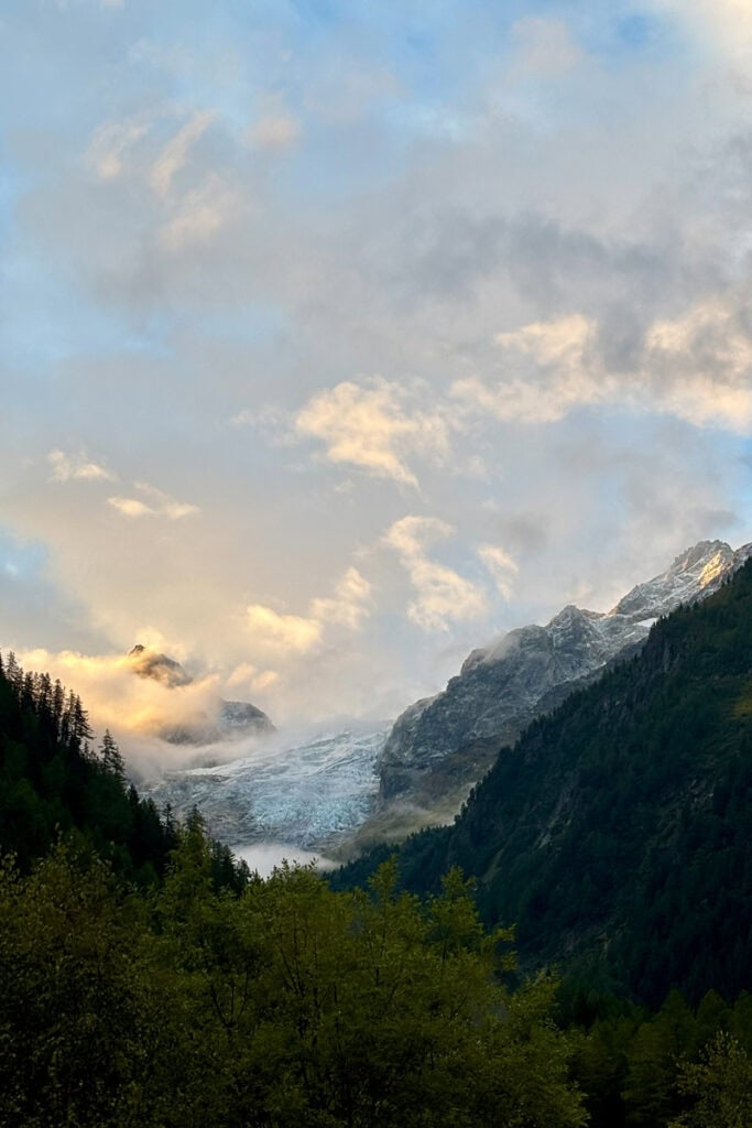 Early morning light on snow-covered mountain peak partially covered by clouds.