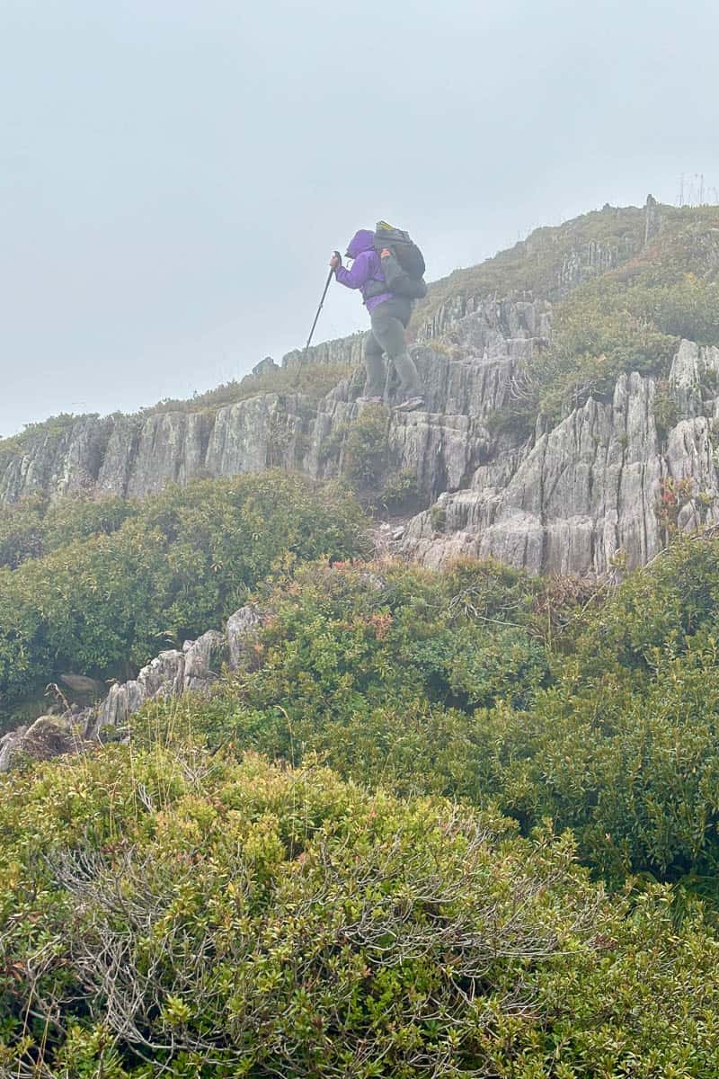 Backpacker hiking through fog along narrow rocky ledge on Tour du Mont Blanc Stage 9.