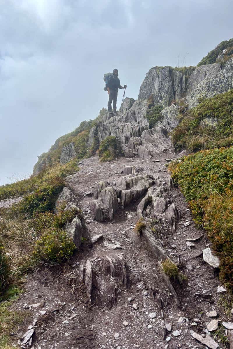 Backpacker standing at top of rocky trail in the fog.