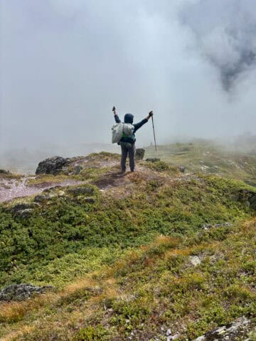 Backpacker with arms raised triumphantly toward foggy view.