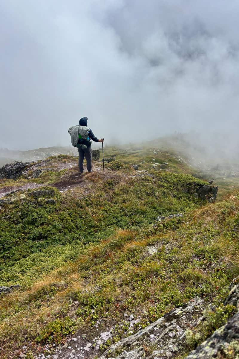 Backpacker looking out over a bank of thick fog obscuring the view.