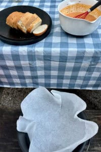 Sliced bread loaf next to bowl of pumpkin custard mixture and Dutch oven lined with parchment paper.