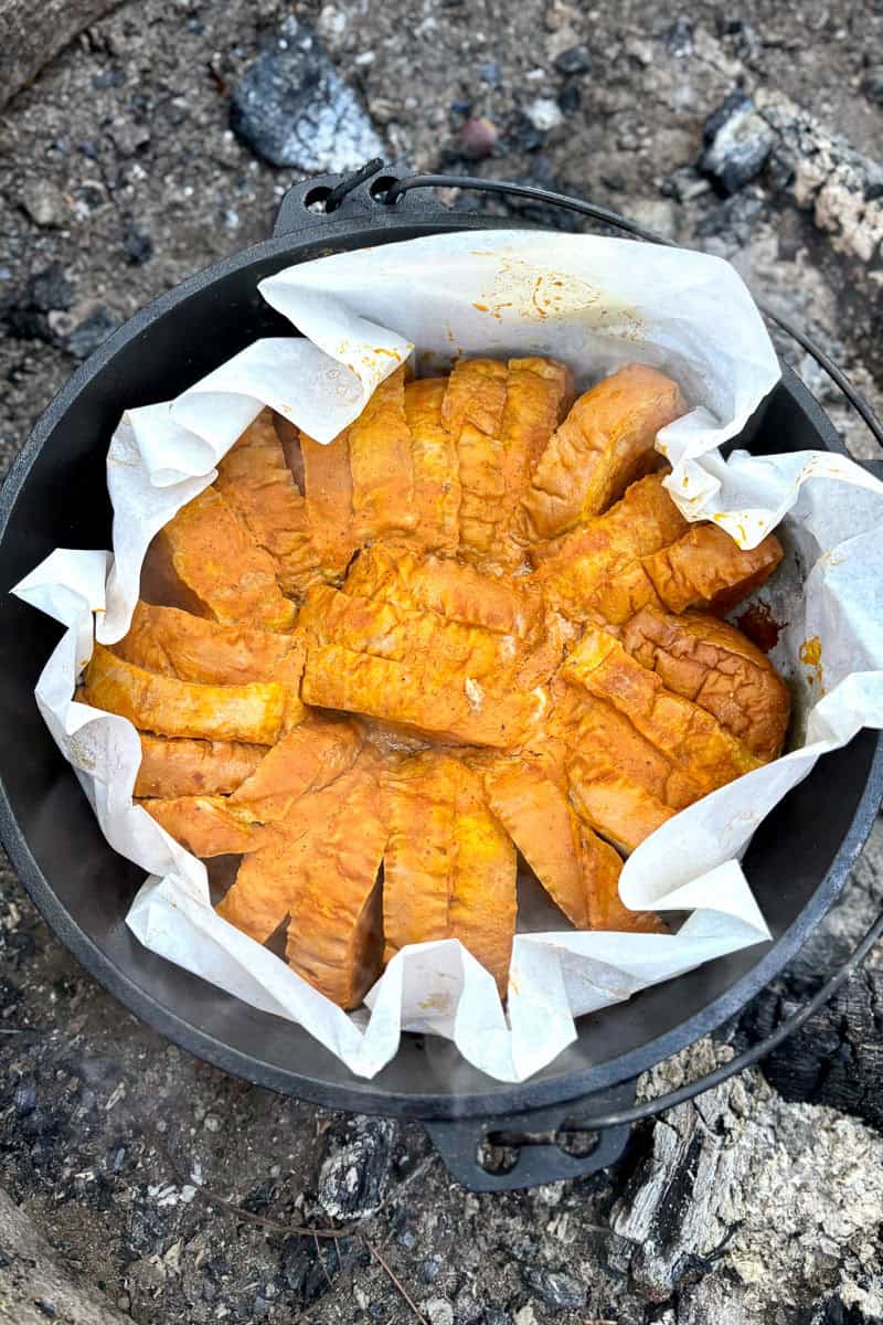 Dutch oven lined with parchment paper and filled with campfire baked French toast.