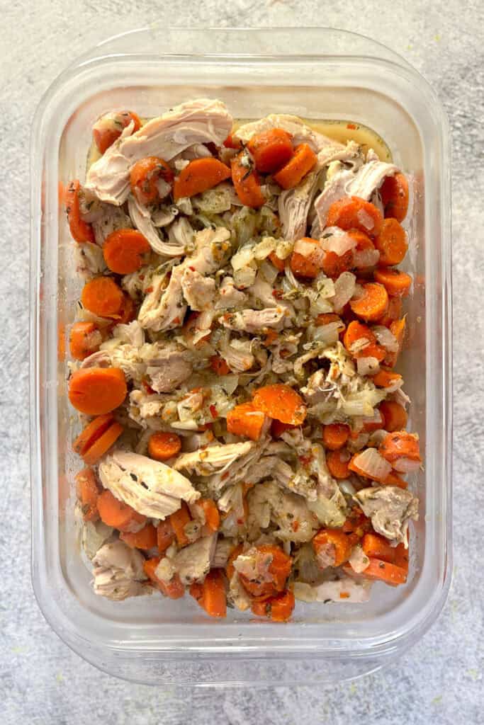 Cooked chicken, carrots, and onions in storage container.
