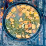 Cast-iron dutch oven with sweet potato chunks, spinach, quinoa and broth.