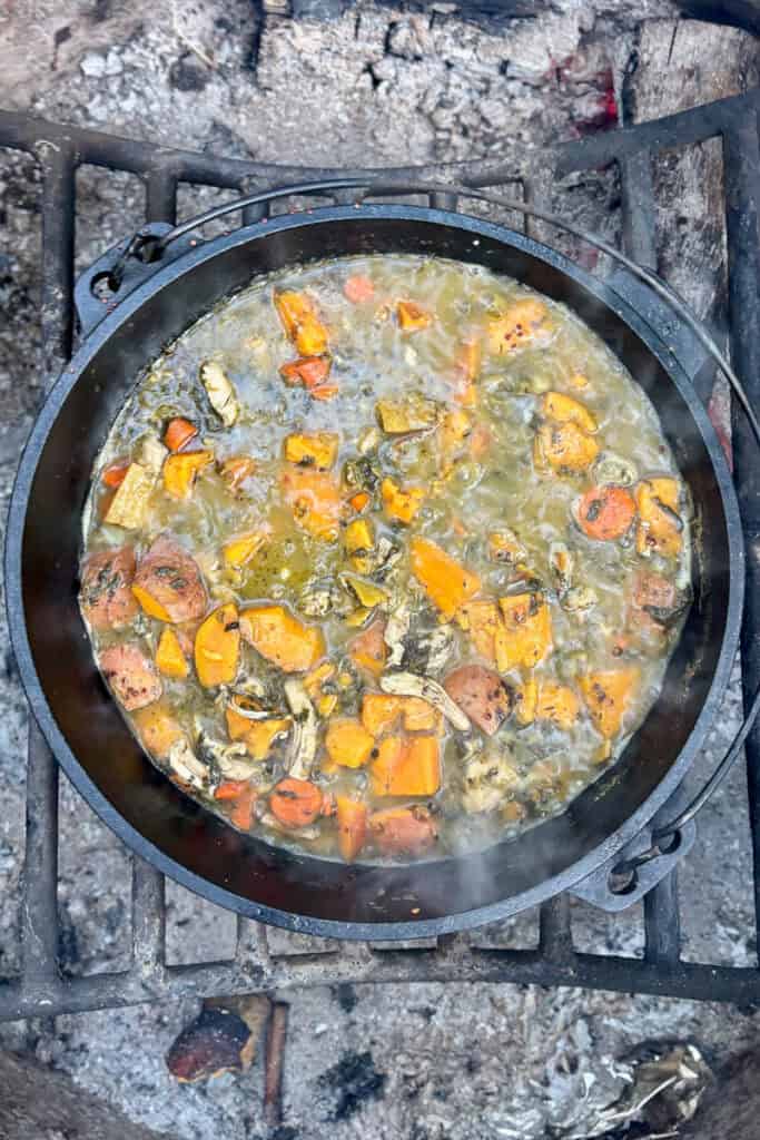 Cast-iron dutch oven filled with cooked sweet potatoes, carrots, chicken, spinach and quinoa.