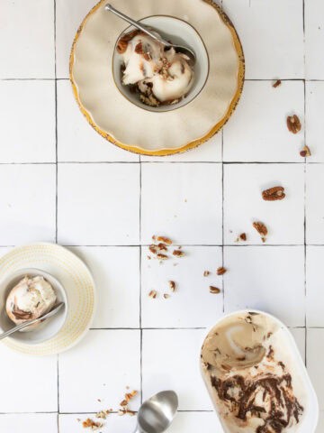 Carton and bowls of bourbon ice cream with chocolate swirl topped with pecans.